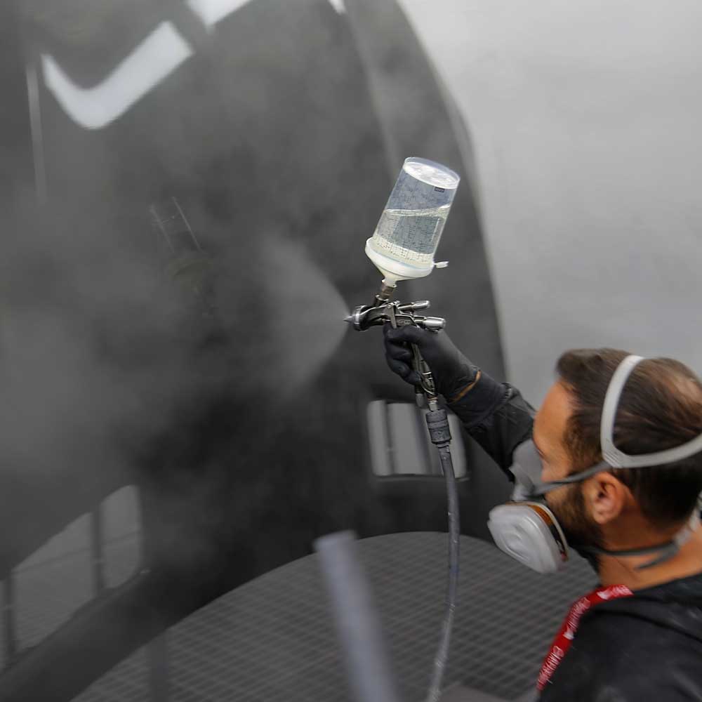 jakobson-dienstleistungen-fahrzeug-kleinserien-lackierung Dienstleistungen-Fahrzeug- und Kleinserienlackierung-Mitarbieter lackiert eine schwarze Motorhaube