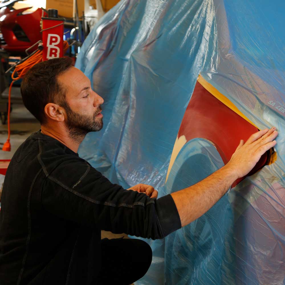 jakobson-dienstleistungen-aufbereitung-leasingrückläufer Dienstleistungen-Aufbereitung von Leasingrückläufern-Mitarbeiter klebt einen Bereich eines roten Autos ab