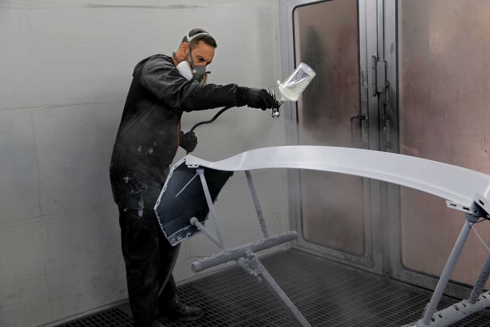 Fahrzeug- und Kleinserienlackierung-Mitarbeiter lackiert eine weiße Heckschürze