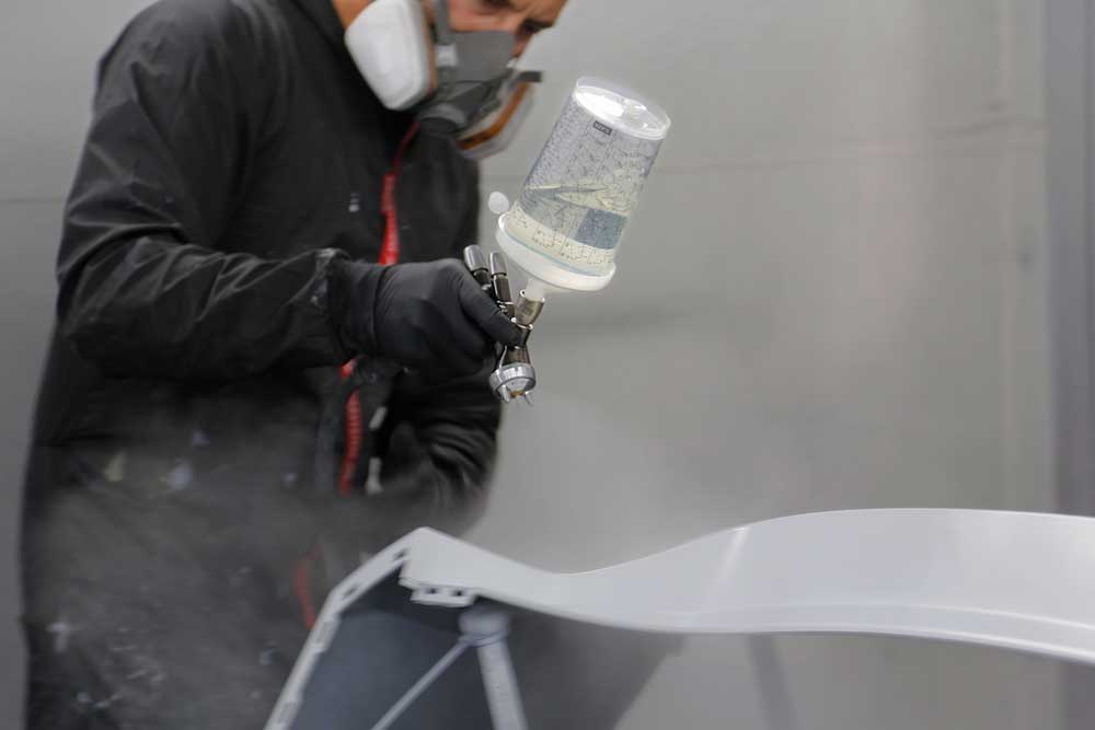 Fahrzeug- und Kleinserienlackierung-Nahaufnahme eines Mitarbeiters, der eine weiße Heckschürze lackiert
