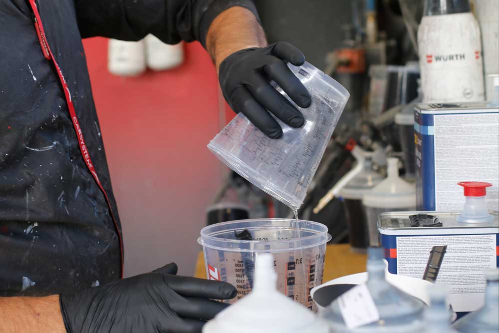 Fahrzeug- und Kleinserienlackierung-Mitarbeiter mischt Lack in einem Behältnis