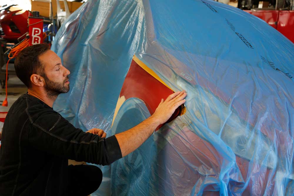 Aufbereitung von Leasingrückläufern-Mitarbeiter klebt einen Bereich eines roten Autos ab