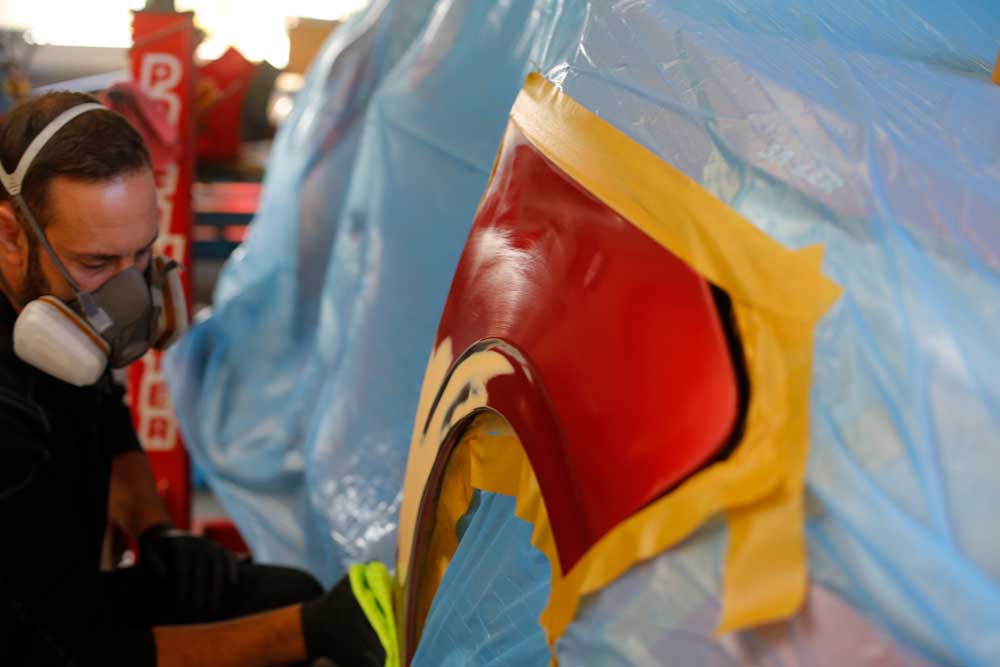 Aufbereitung von Leasingrückläufern-Mitarbeiter mit einer Lackiermaske reinigt den abgeklebten Bereich mit einem grünen Tuch