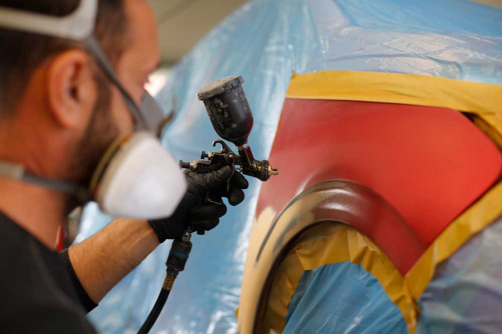 Aufbereitung von Leasingrückläufern-Mitarbeiter mit einer Lackiermaske lackiert den abgeklebten Teil des roten Autos